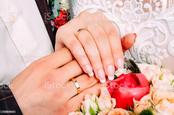 Newly married couple holding hands together wearing wedding rings with beautiful bridal manicure